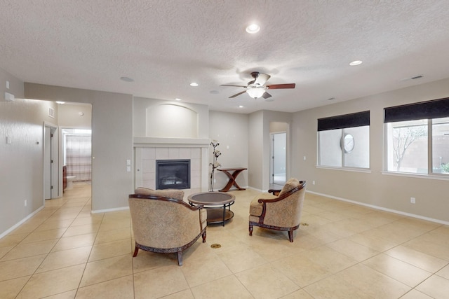 tiled living room featuring a tile fireplace, a textured ceiling, and ceiling fan