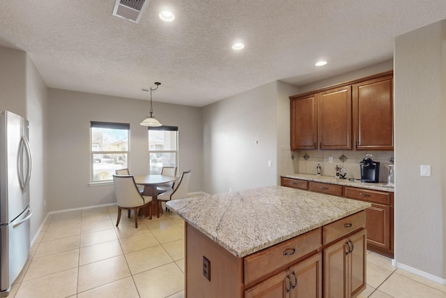 kitchen featuring stainless steel refrigerator, a kitchen island, pendant lighting, light stone countertops, and backsplash