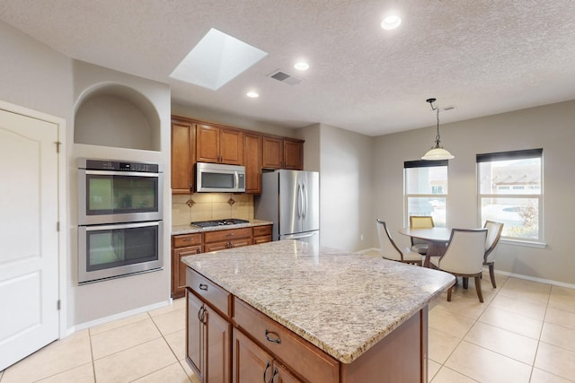 kitchen featuring light tile patterned floors, stainless steel appliances, a center island, decorative backsplash, and decorative light fixtures