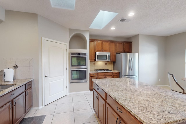 kitchen featuring light tile patterned floors, a skylight, stainless steel appliances, a center island, and decorative backsplash