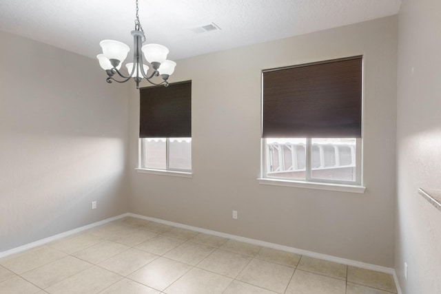 spare room with an inviting chandelier, a textured ceiling, and light tile patterned flooring