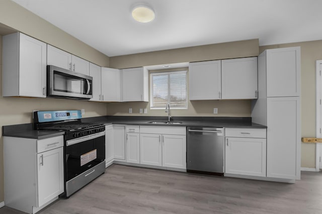 kitchen with stainless steel appliances, sink, white cabinets, and light wood-type flooring