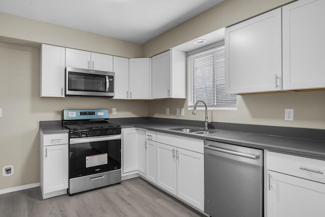 kitchen with appliances with stainless steel finishes, sink, white cabinets, and light hardwood / wood-style floors