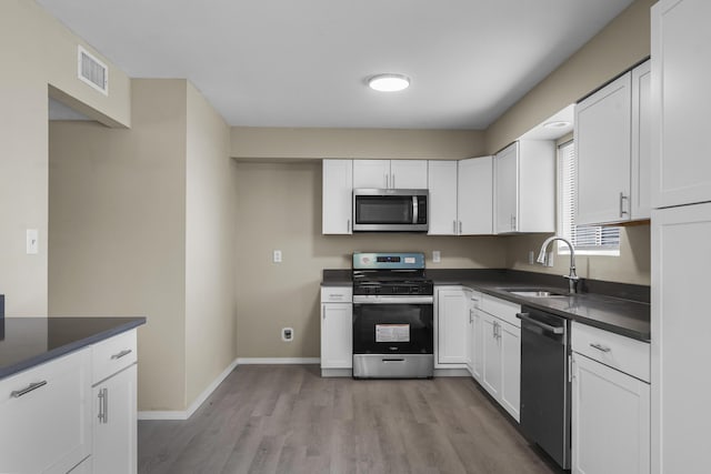 kitchen featuring appliances with stainless steel finishes, sink, white cabinets, and light hardwood / wood-style flooring