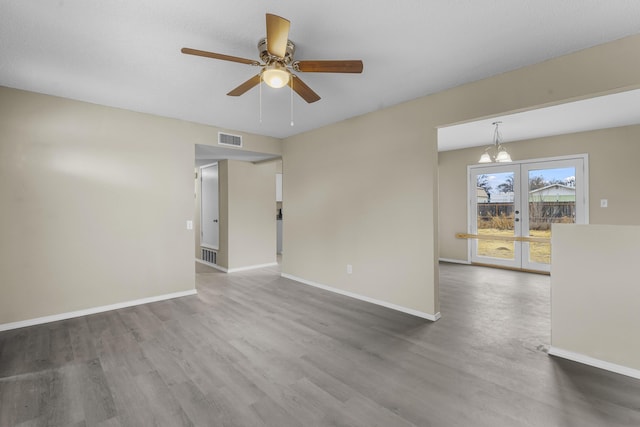 empty room featuring ceiling fan with notable chandelier, hardwood / wood-style floors, and french doors