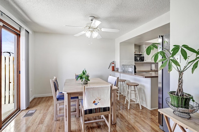 dining room with ceiling fan, a textured ceiling, and light wood-type flooring