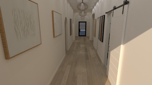 corridor featuring a barn door, light wood-style flooring, arched walkways, and baseboards