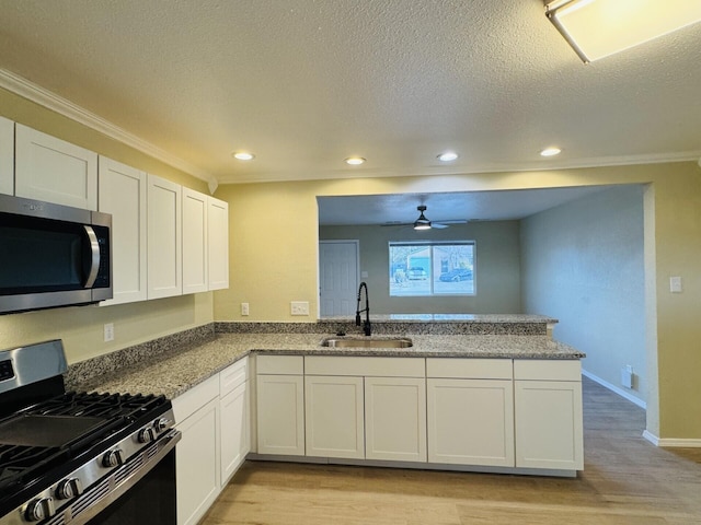 kitchen with a sink, stainless steel appliances, a peninsula, light wood finished floors, and ceiling fan