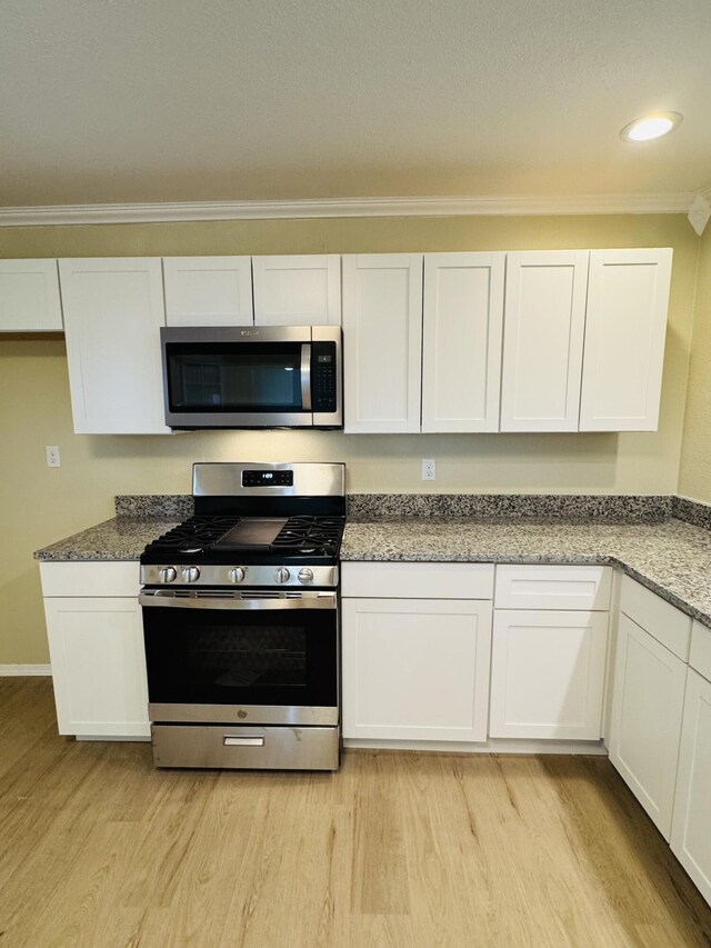 kitchen with light wood-type flooring, appliances with stainless steel finishes, and white cabinetry