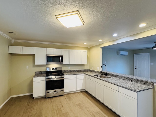 kitchen featuring light wood finished floors, a peninsula, a sink, stainless steel appliances, and white cabinets