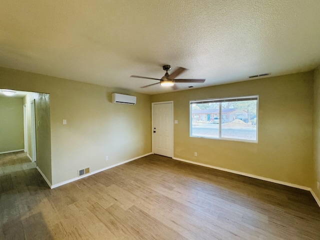 empty room featuring baseboards, ceiling fan, a wall mounted air conditioner, wood finished floors, and a textured ceiling