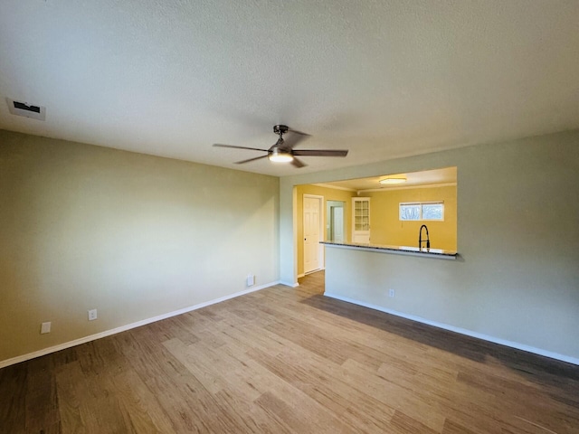 empty room with visible vents, a sink, wood finished floors, baseboards, and ceiling fan