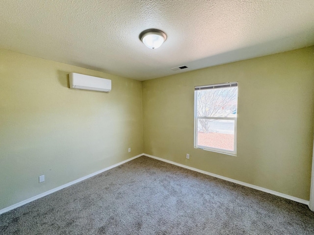 spare room featuring carpet flooring, a textured ceiling, a wall mounted air conditioner, and baseboards