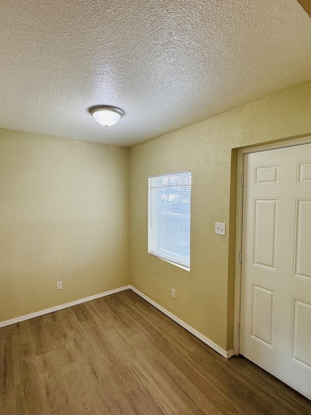 empty room featuring a textured ceiling, baseboards, and wood finished floors