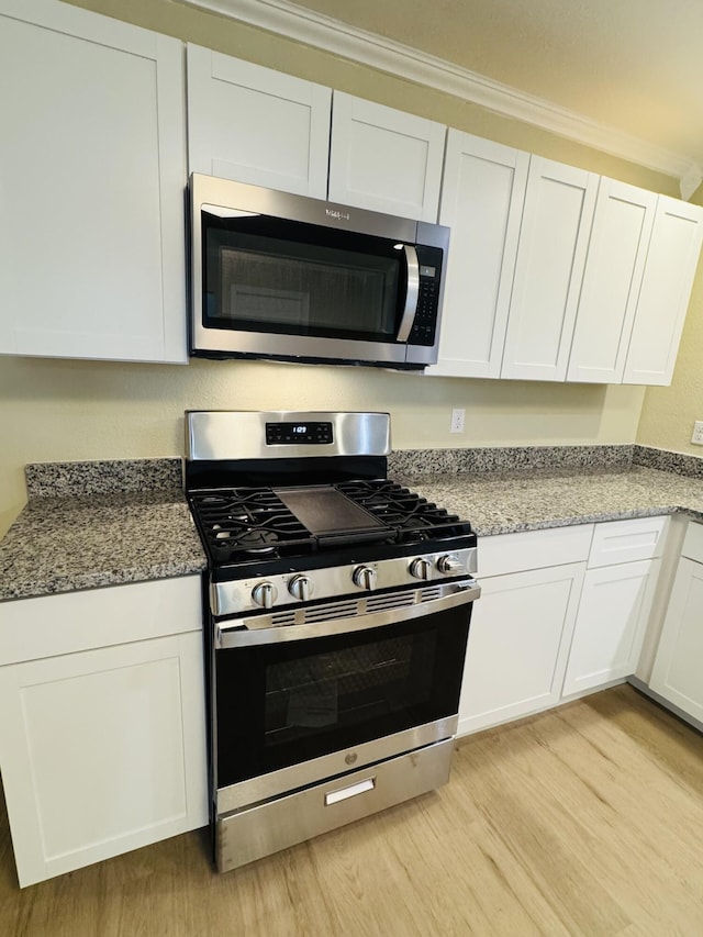 kitchen with stone countertops, stainless steel appliances, white cabinetry, and light wood finished floors