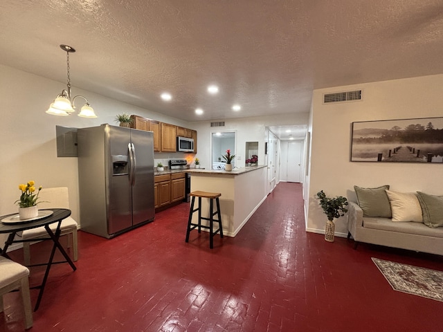 kitchen featuring a breakfast bar, decorative light fixtures, appliances with stainless steel finishes, brown cabinetry, and a peninsula