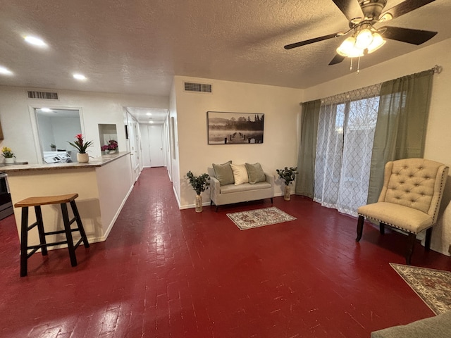 living room with a ceiling fan, visible vents, a textured ceiling, and baseboards