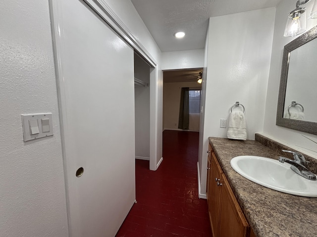 bathroom with a textured ceiling, brick floor, a ceiling fan, vanity, and baseboards