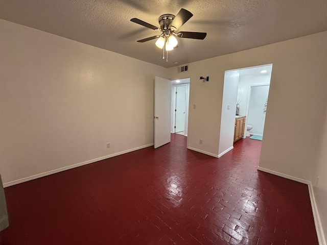 spare room featuring ceiling fan, a textured ceiling, brick floor, visible vents, and baseboards