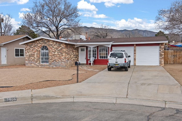 ranch-style house with brick siding, an attached garage, a mountain view, fence, and driveway