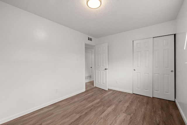 unfurnished bedroom featuring hardwood / wood-style floors, a closet, and a textured ceiling