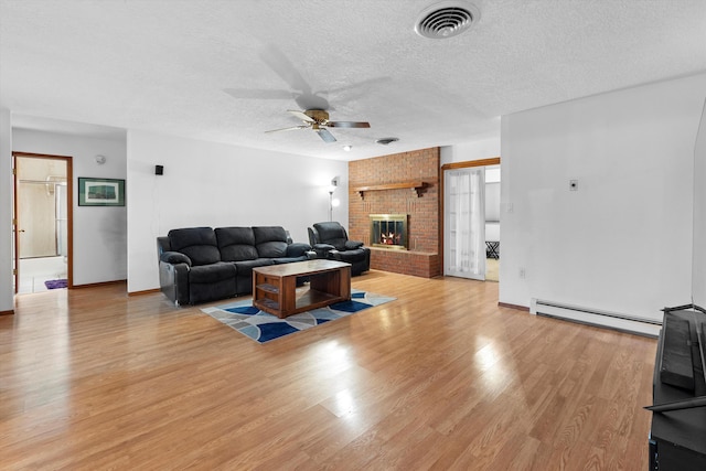 living room featuring a baseboard heating unit, ceiling fan, light hardwood / wood-style floors, a brick fireplace, and a textured ceiling