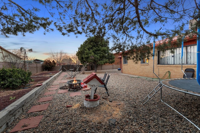 yard at dusk featuring a trampoline and an outdoor fire pit