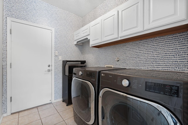 clothes washing area with light tile patterned floors, cabinets, and washing machine and clothes dryer