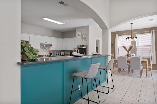 kitchen featuring light tile patterned floors, white cabinetry, decorative backsplash, decorative light fixtures, and stainless steel oven