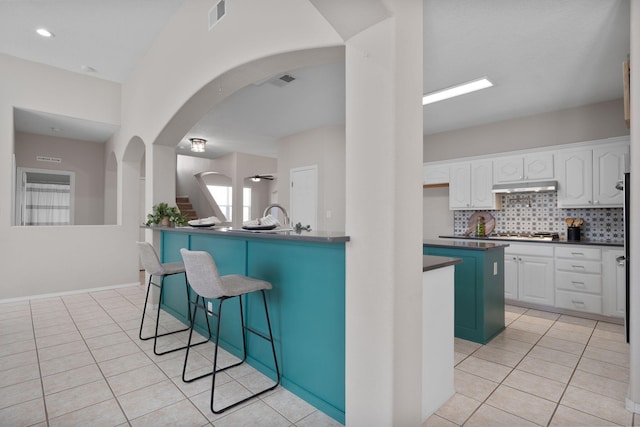 kitchen with light tile patterned flooring, tasteful backsplash, white cabinets, a kitchen bar, and a center island