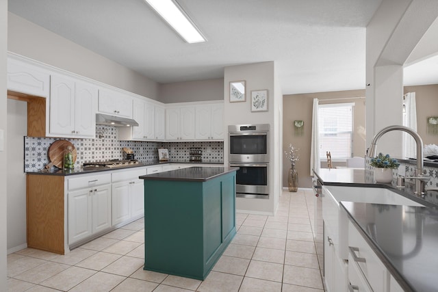 kitchen featuring appliances with stainless steel finishes, white cabinets, a kitchen island, decorative backsplash, and light tile patterned flooring