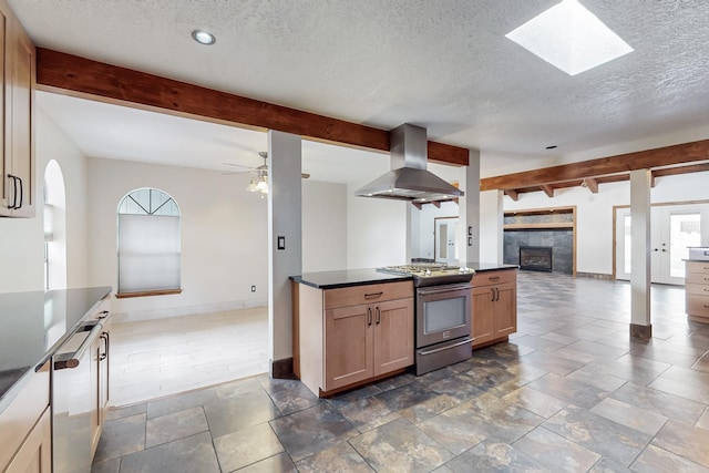 kitchen with beamed ceiling, dark countertops, open floor plan, stainless steel range with gas cooktop, and wall chimney range hood