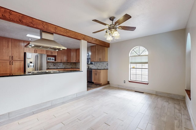 kitchen featuring dark countertops, range hood, appliances with stainless steel finishes, brown cabinetry, and decorative backsplash