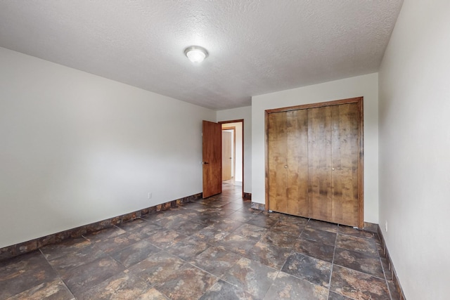 unfurnished bedroom featuring a closet, a textured ceiling, stone finish flooring, and baseboards