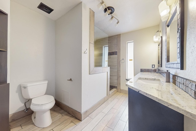 bathroom featuring visible vents, a walk in shower, wood tiled floor, toilet, and vanity