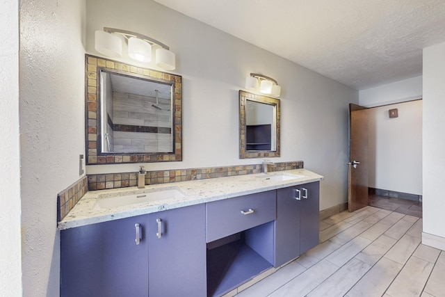 full bath with double vanity, a textured ceiling, baseboards, and a sink