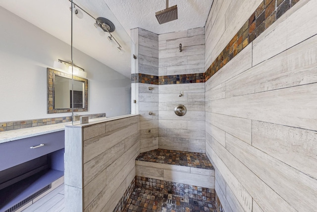 full bathroom with a textured ceiling, tiled shower, and vanity