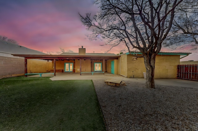 back of house at dusk with a yard, a patio area, fence, and a chimney