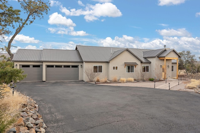 view of front of house with a garage, stucco siding, metal roof, and aphalt driveway