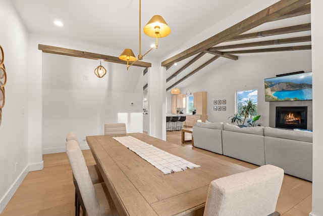 dining area with a warm lit fireplace, baseboards, lofted ceiling with beams, light wood-style floors, and recessed lighting