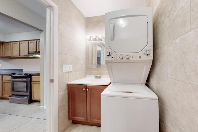 laundry room featuring light tile patterned flooring, stacked washer and dryer, sink, and tile walls