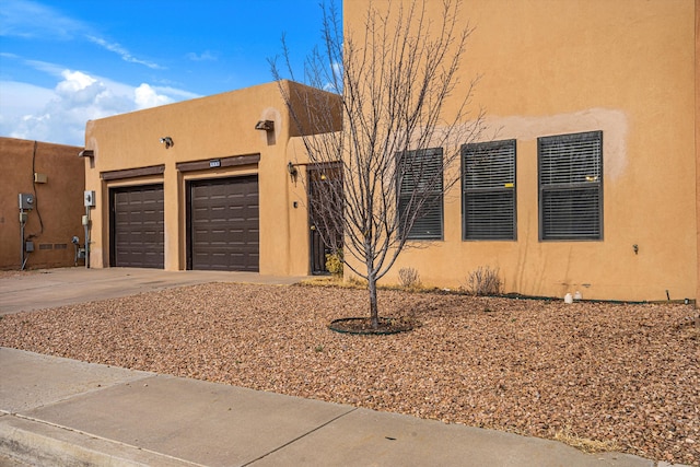 pueblo revival-style home featuring driveway, an attached garage, and stucco siding