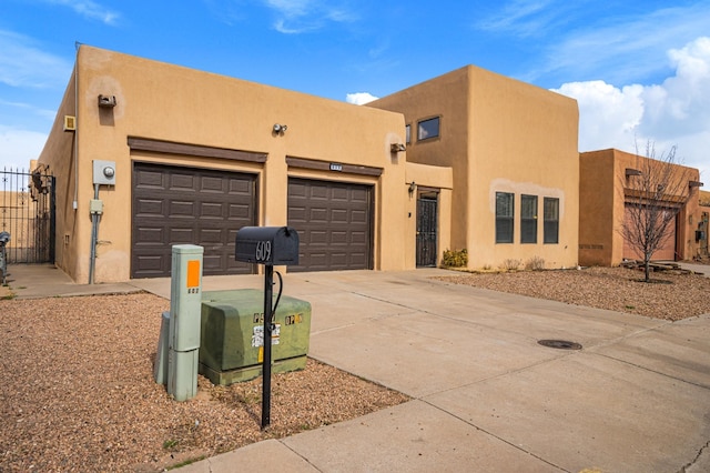 pueblo-style house featuring a garage, driveway, fence, and stucco siding