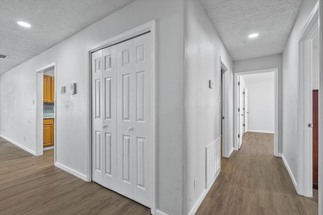 corridor featuring a textured ceiling, wood finished floors, visible vents, and baseboards