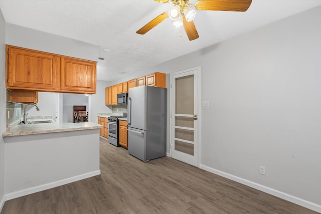 kitchen with a textured ceiling, wood finished floors, a sink, light countertops, and appliances with stainless steel finishes