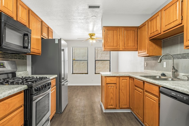 kitchen featuring dark wood-style flooring, light countertops, appliances with stainless steel finishes, brown cabinetry, and a sink