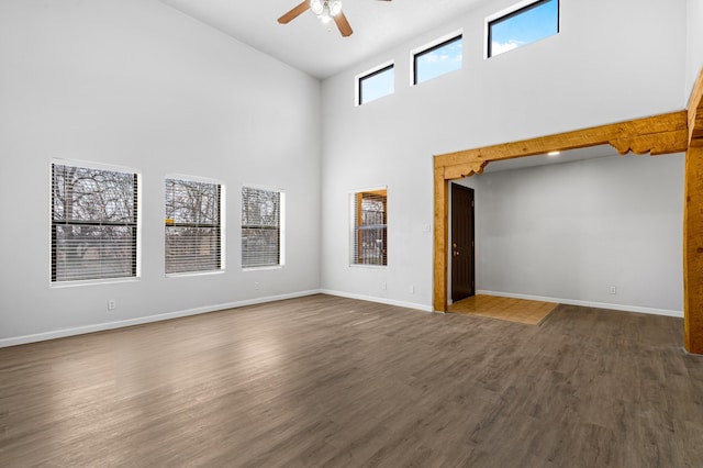 empty room with a towering ceiling, ceiling fan, baseboards, and dark wood-type flooring