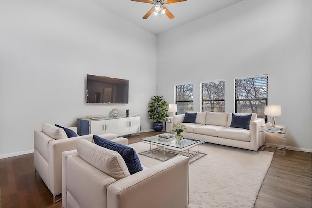 living room with a towering ceiling, a ceiling fan, baseboards, and wood finished floors