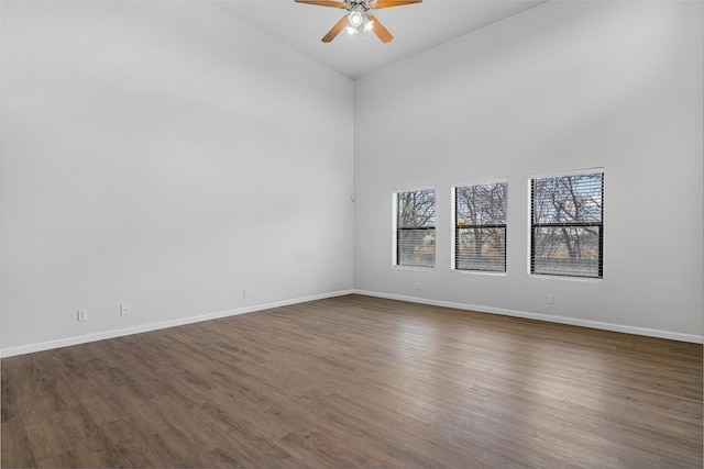 unfurnished room featuring dark wood-style floors, a towering ceiling, baseboards, and a ceiling fan