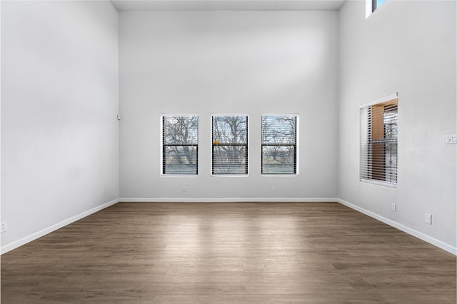 empty room with baseboards, a high ceiling, and wood finished floors